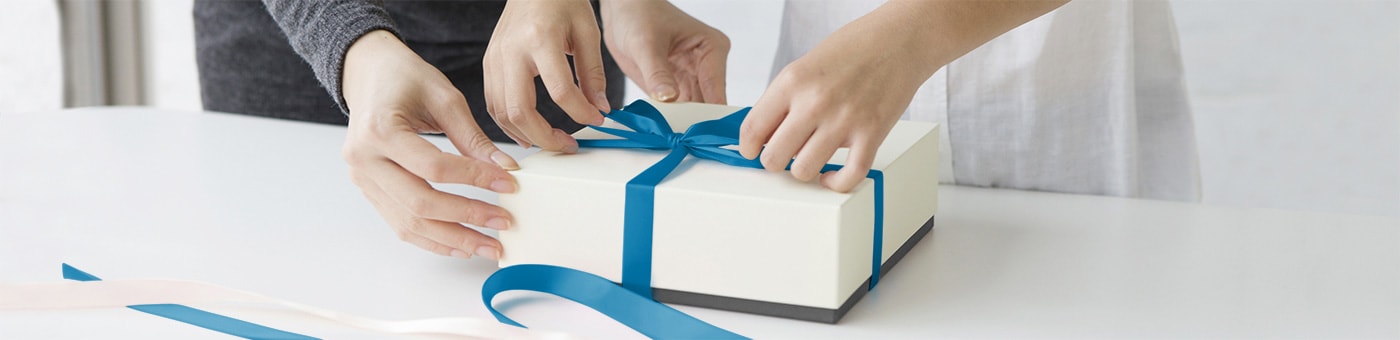 Hände verpacken ein weißes Geschenk mit blauer Schleife